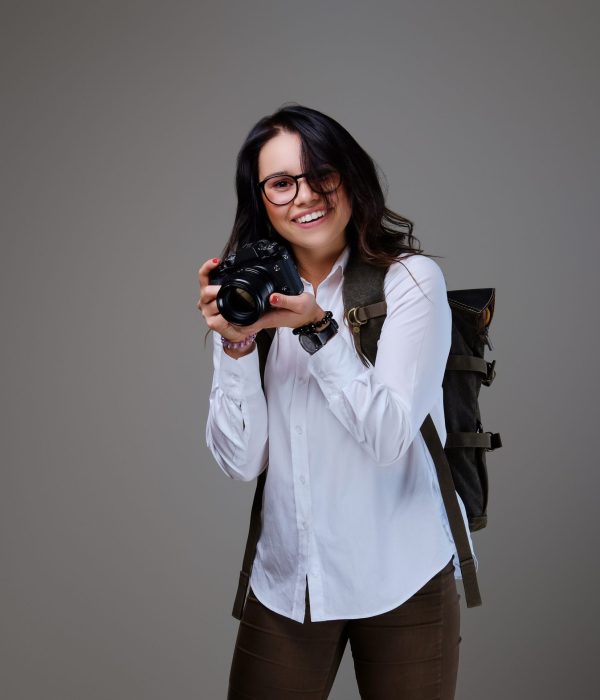 Positive female tourist with photo camera and travel backpack.